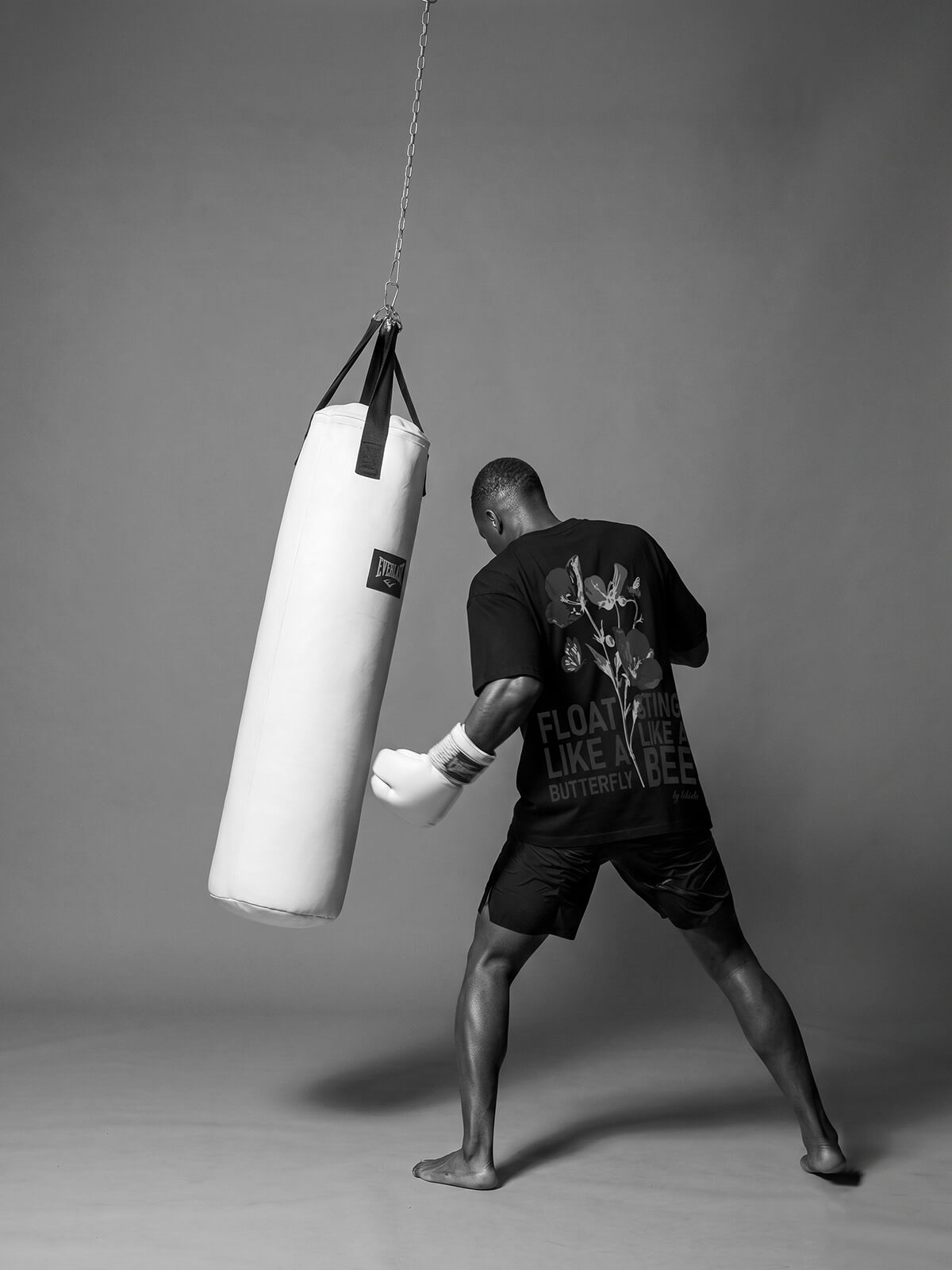 Boxer training with a heavy bag in a minimal studio setting wearing a t-shirt with “Float like a butterfly, sting like a bee” print