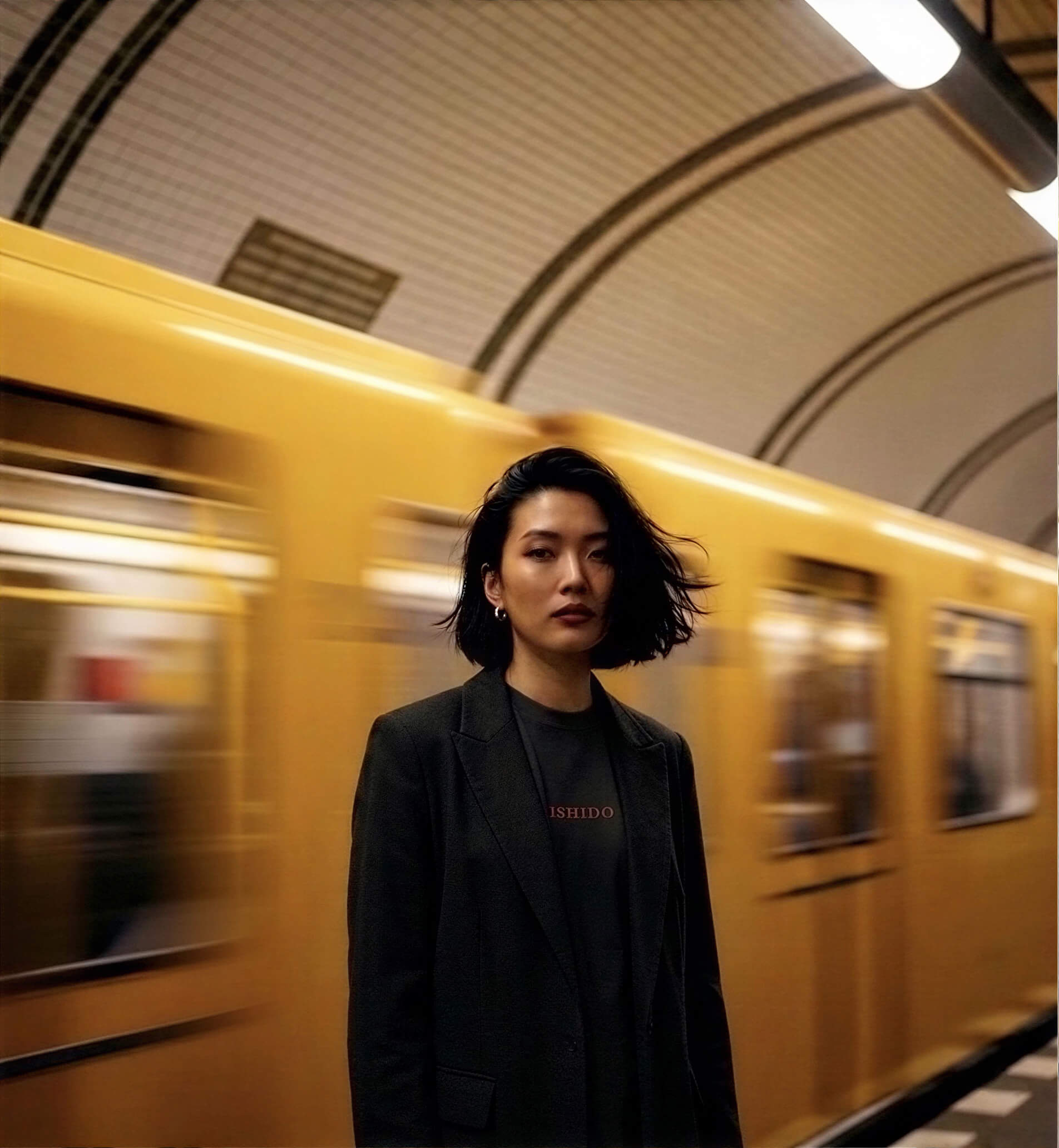 Woman wearing Bshidō apparel standing in a subway station with a moving train in the background