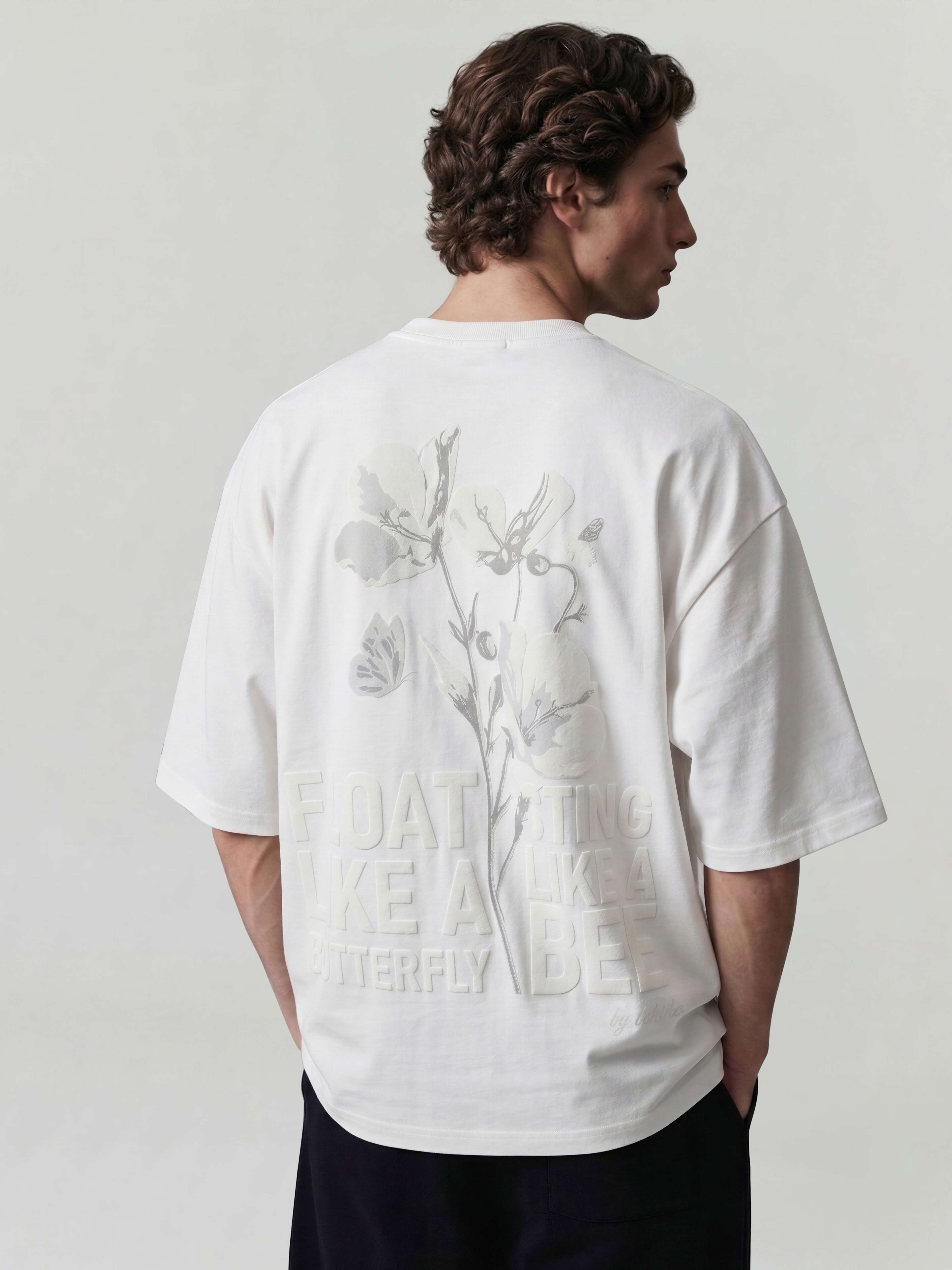 White oversized Bshido t-shirt back angled view with floral graphic and “Float like a butterfly sting like a bee” print
