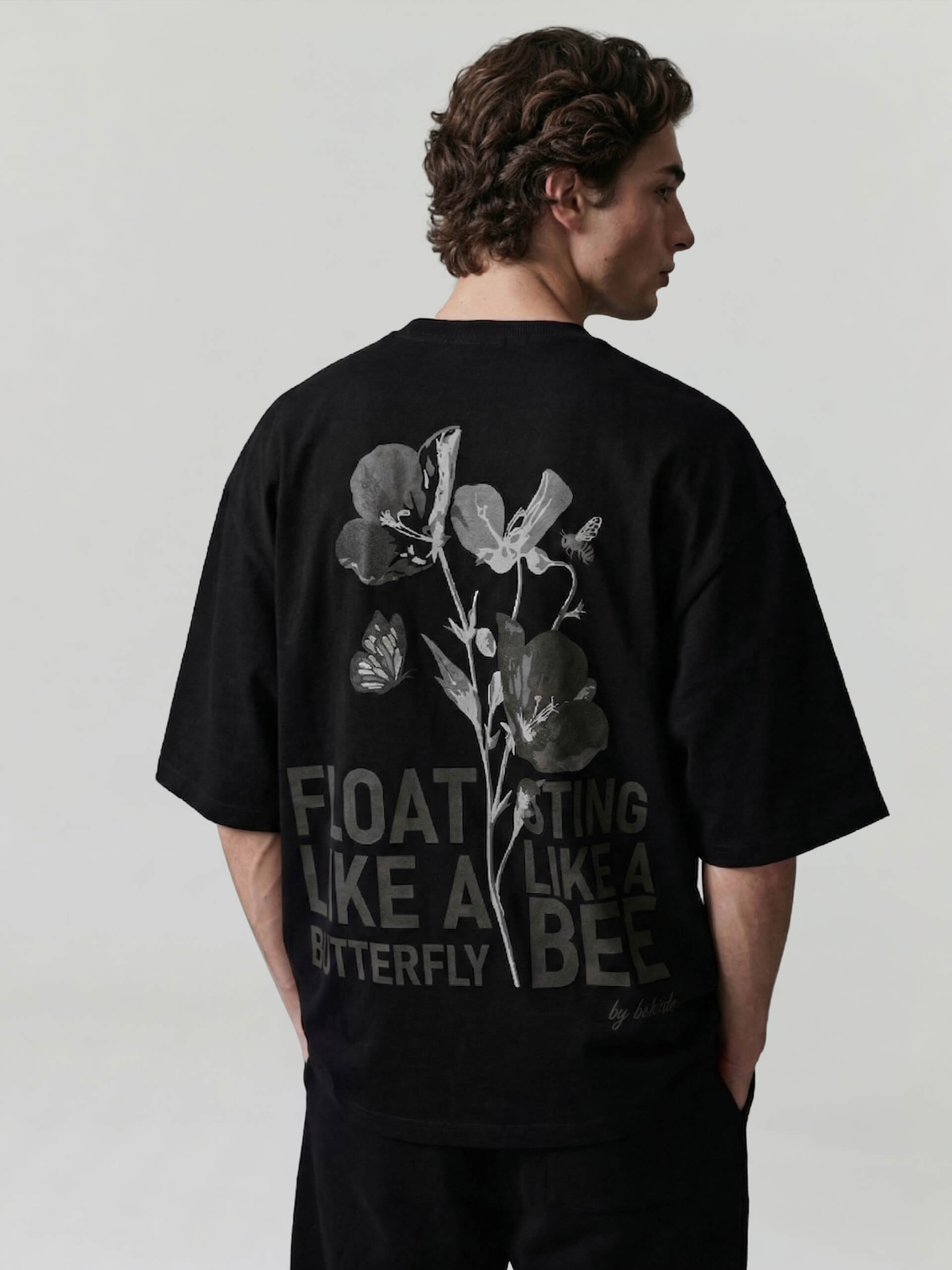 Black oversized Bshido t-shirt back angled view with floral graphic and “Float like a butterfly sting like a bee” print