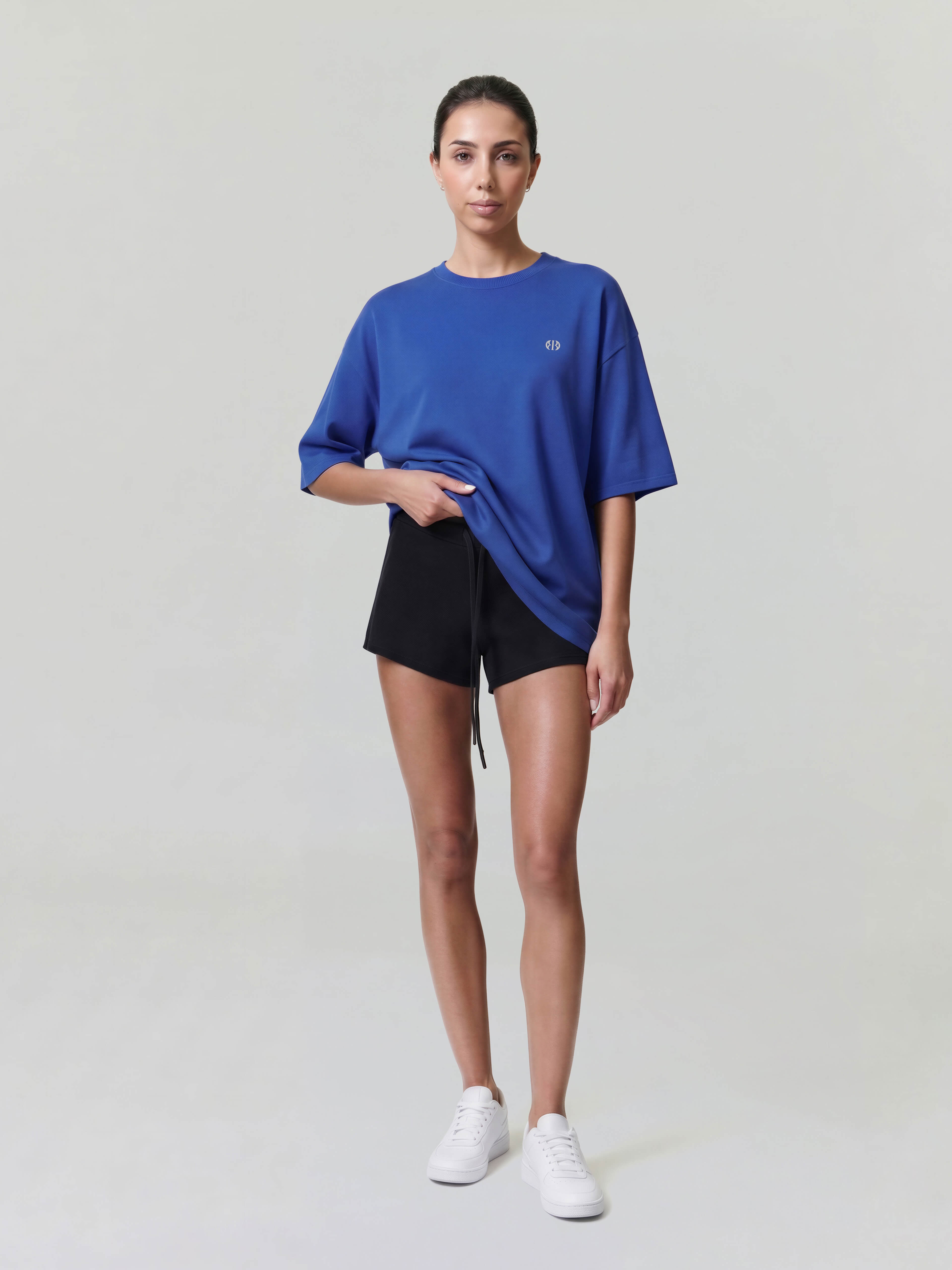 Female model wearing blue oversized Bshido t-shirt front full body view with minimal logo and black shorts