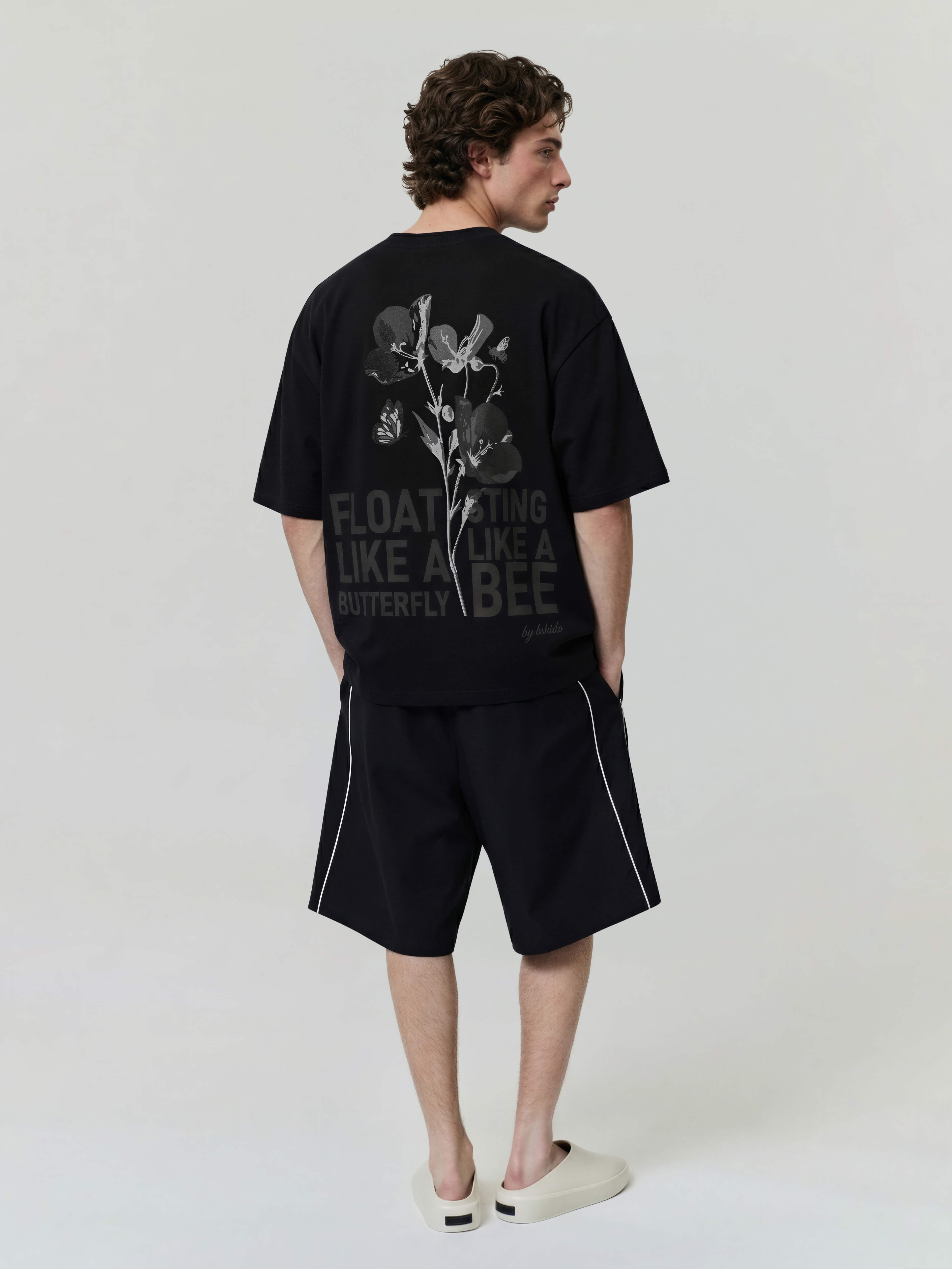 Full body back view of black oversized Bshido t-shirt with floral graphic and “Float like a butterfly sting like a bee” print