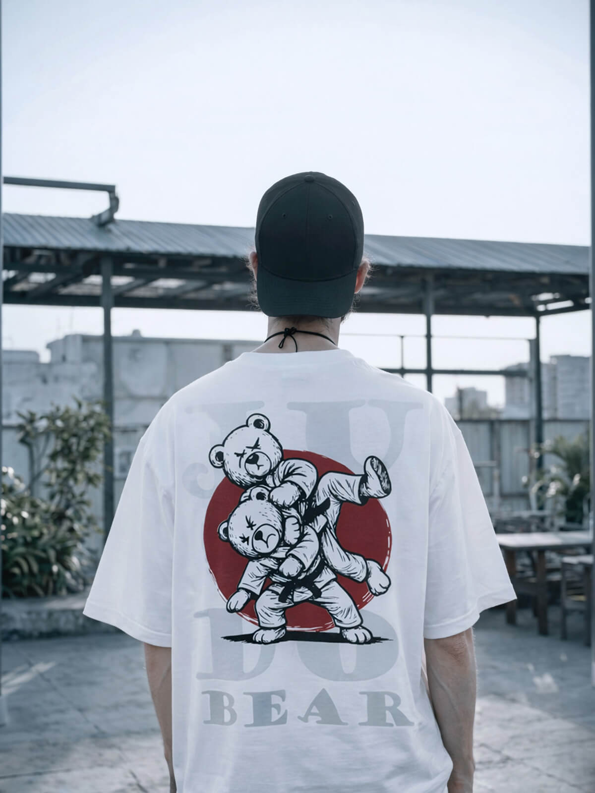 Person wearing a white Bshidō t-shirt with a judo bear graphic on the back in an urban setting.