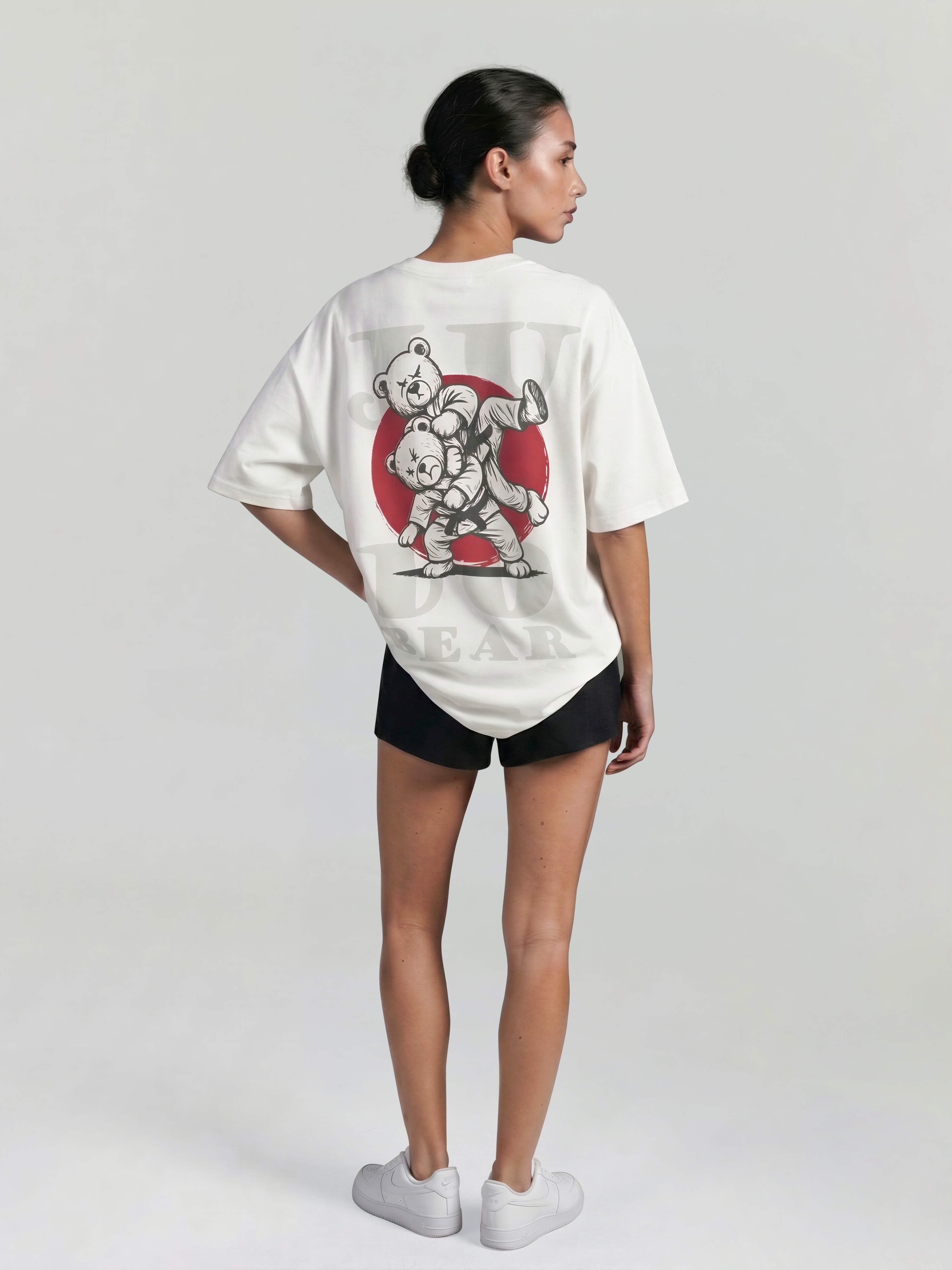 Female model wearing white oversized Bshido t-shirt back angled view with judo bear graphic and red circle print