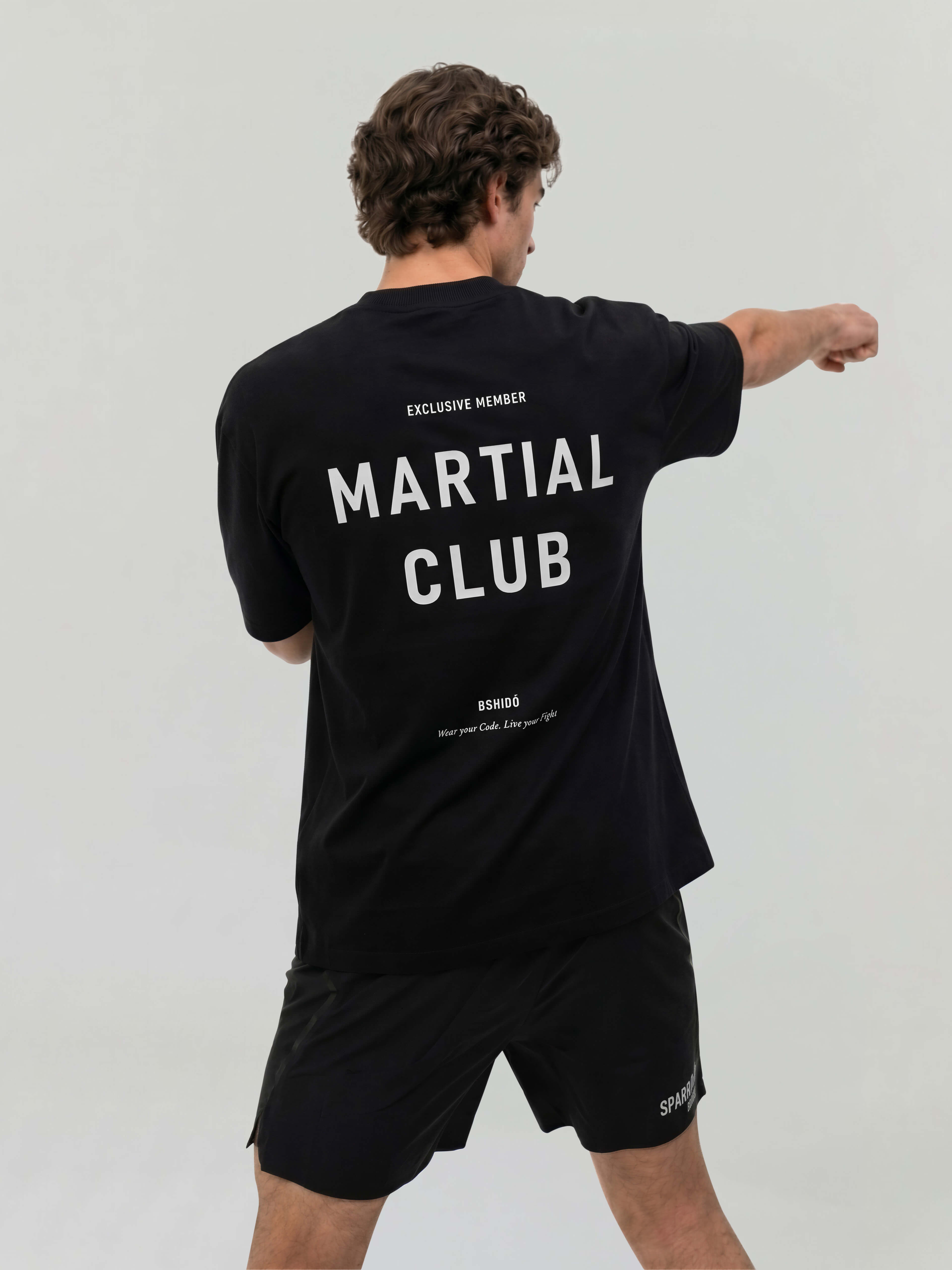 Male model in action pose wearing black oversized Bshido t-shirt showing “Martial Club” back print