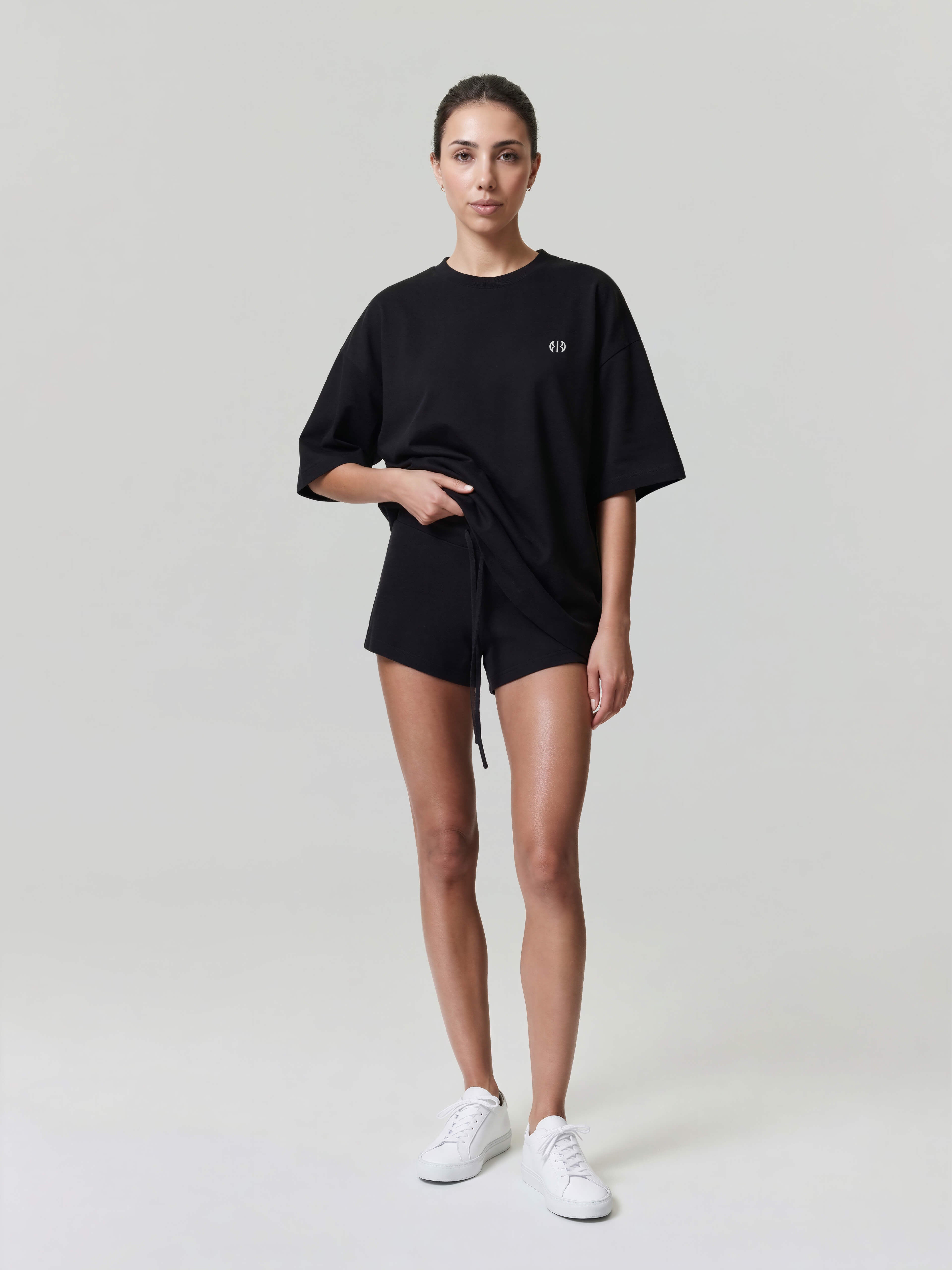Female model wearing black oversized Bshido t-shirt front full body view with minimal logo and black shorts