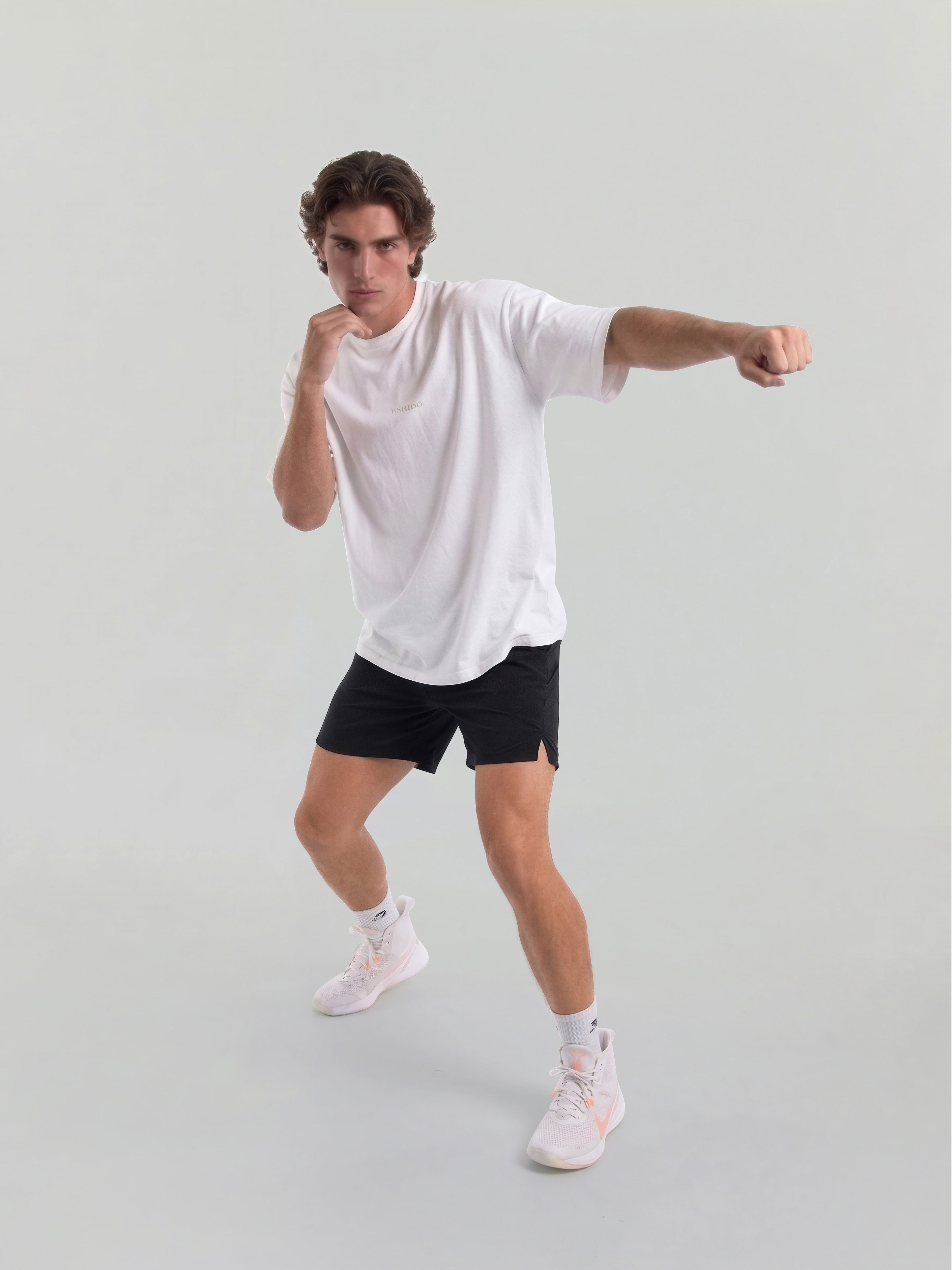 Male model wearing white oversized Bshido t-shirt front view in fighting stance with black shorts